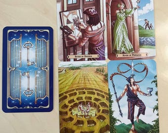 May include: A set of five tarot cards featuring illustrated scenes. One card shows a blue back with two keys. The others depict the Seven of Swords, Seven of Pentacles, XIX The Sun with a labyrinth, and 1 The Magician balancing a sword on a nose.