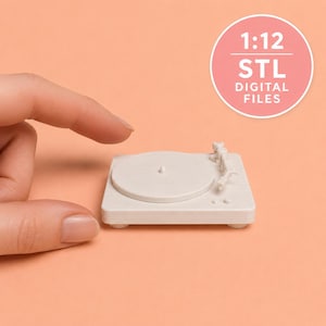 Könnte beinhalten: Ein weißes, 3D-gedrucktes Miniatur-Plattenspielermodell mit rundem Plattenteller und Tonarm. Eine kreisförmige rosa Grafik in der oberen rechten Ecke enthält den weißen Text 1:12 STL DIGITAL FILES auf einem einfarbigen pfirsichfarbenen Hintergrund.