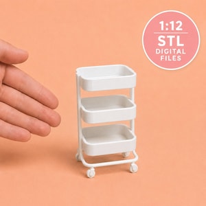 May include: A white three-tiered rolling utility cart in 1:12 scale. The miniature storage unit features three rectangular shelves with rounded corners, supported by a frame on four small wheels. A circular graphic displays the text 1:12 STL DIGITAL FILES.