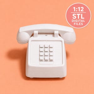 May include: A white 1:12 scale telephone model with a handset resting on a base featuring a twelve-button keypad. The object is labeled with the text 1:12 STL DIGITAL FILES in a circular badge, indicating it is a digital file for 3D printing.