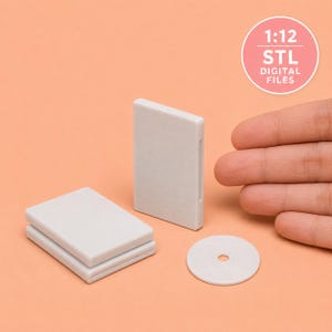 Puede incluir: Un conjunto de cajas de DVD en miniatura de plástico gris a escala 1:12 y un disco circular. Los artículos están en blanco y tienen un acabado mate liso. Un gráfico circular rosa en la esquina superior derecha contiene el texto 1:12 STL DIGITAL FILES.
