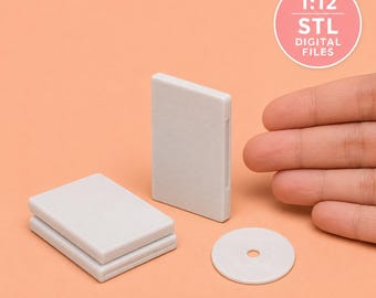 May include: A set of miniature 1:12 scale grey plastic DVD cases and a circular disc. The items are blank and feature a smooth, matte finish. A circular pink graphic in the upper right corner contains the text 1:12 STL DIGITAL FILES.