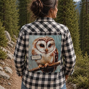 May include: A black and white buffalo plaid button-down shirt featuring a large, rectangular patch on the back. The patch displays a detailed painting of a brown and white owl perched on a branch, with a small label reading "live, love, hoot."