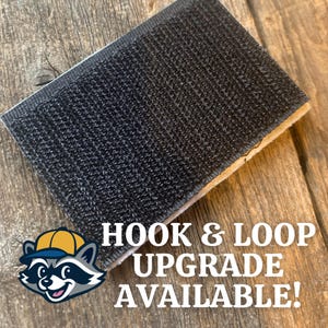 K&ouml;nnte beinhalten: Ein rechteckiges St&uuml;ck schwarzer Klettverschluss mit wei&szlig;em Rand. Der Text "HOOK & LOOP UPGRADE AVAILABLE!" wird in Wei&szlig; zusammen mit einem Cartoon-Waschb&auml;ren mit Hut angezeigt.