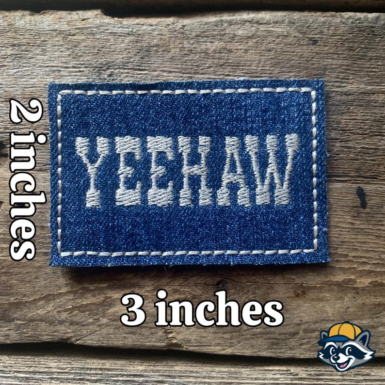 K&ouml;nnte beinhalten: Ein rechteckiger Denim-Aufn&auml;her mit dem Wort "YEEHAW" in Wei&szlig; gestickt. Der Aufn&auml;her ist ca. 7,6 cm lang und 5,1 cm breit, mit einem wei&szlig;en, gen&auml;hten Rand. Er liegt auf einem rustikalen Holzgrund.