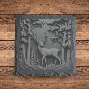 May include: A gray slate coaster with a carved design of a deer standing in a forest. The deer is facing the right side of the image and has large antlers. The trees in the background are tall and slender.