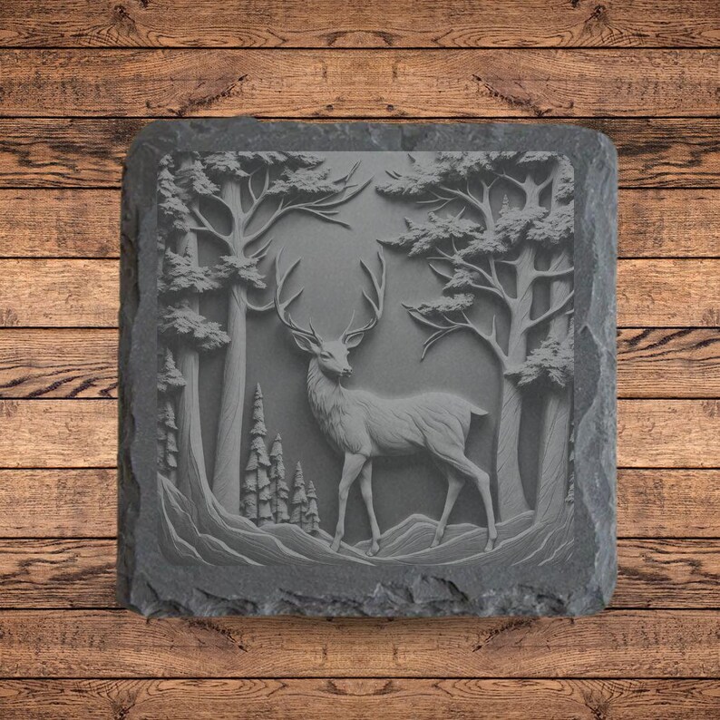 May include: A gray slate coaster with a carved design of a deer standing in a forest. The deer is facing the right side of the image and has large antlers. The trees in the background are tall and slender.