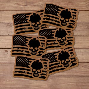 May include: A collection of brown and black stickers featuring a distressed American flag design with a skull wearing a hard hat. The stickers have a weathered look, with the flag's stars and stripes and the skull's details clearly visible.