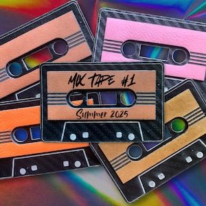 May include: A collection of colorful cassette tapes with the text "MIX TAPE #1 Summer 2025" on the central tape. The tapes are in shades of orange, pink, and brown, with a black and silver frame. The background has a rainbow holographic effect.