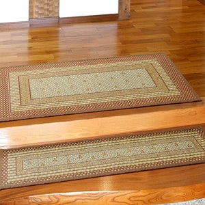 Könnte beinhalten: Zwei braune und beige gemusterte Fußmatten mit geometrischem Design. Die größere Matte liegt auf einem Holzboden und die kleinere Matte liegt auf einer Holztreppe.