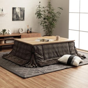 Puede incluir: Un futón de color marrón y gris a cuadros con una mesa de madera y una almohada a rayas grises y blancas. El futón está sobre una alfombra gris con un patrón de diamantes.