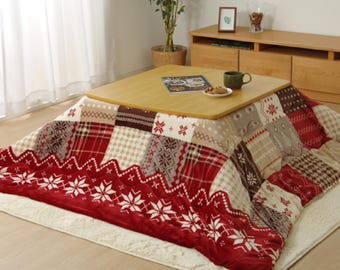 Puede incluir: Una manta eléctrica con calefacción roja y blanca con una mesa de madera en la parte superior. La manta tiene un diseño de patchwork con copos de nieve y patrones geométricos.