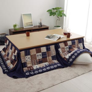 Op de afbeelding: Een houten tafel met daaronder een blauwe en bruine futon met patroon. De futon heeft een wit kussen erop. Op de tafel staan twee mokken en een tijdschrift.