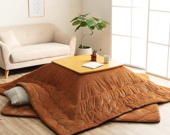 May include: A brown corduroy heated floor mat with a wooden table on top. The mat is folded over on itself and has a pillow on the side. The table has a book and a coffee mug on it.
