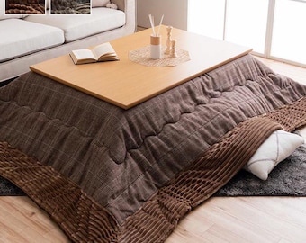 May include: A brown and beige plaid electric heated kotatsu with a wood table top. The kotatsu is on a wood floor with a brown rug underneath.