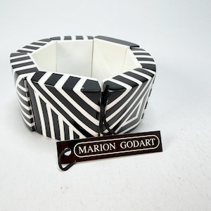 May include: A black and white geometric bracelet with a bold striped pattern. The bracelet is made of segmented pieces and features the brand tag "MARION GODART". The bracelet is a stylish accessory.
