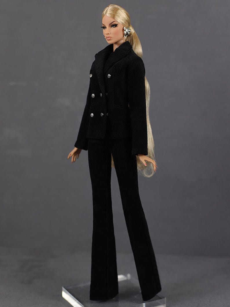 以下が含まれることがあります： ダブルブレストのジャケットとフレアパンツを着用した黒いスーツを着たファッションドール。人形は長い金髪で、銀色のイヤリングをしています。スーツはクラシックなデザインで、さまざまな場面に適しています。