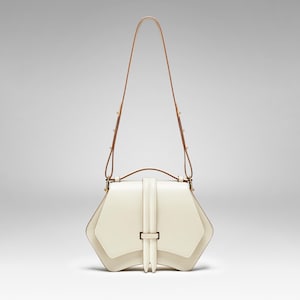 May include: A white leather handbag with a geometric shape and a brown leather strap. The bag has a flap closure with a gold buckle.