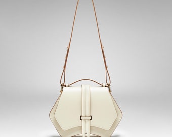 May include: A white leather handbag with a geometric shape and a brown leather strap. The bag has a flap closure with a gold buckle.