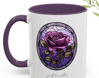 Può includere: Tazza in ceramica bianca con interno e manico viola. La tazza presenta un disegno a vetrata di una rosa viola all'interno di una cornice circolare. Le parole "just breathe" sono scritte in corsivo in basso.
