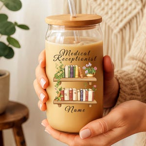 May include: A clear glass tumbler with a wooden lid and straw, filled with a light brown beverage. The tumbler features a design with the words "Medical Receptionist" and "Name" along with illustrations of bookshelves and flowers.