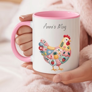 May include: White ceramic mug with a pink handle and interior. The mug features a colorful patchwork chicken design with strawberries, flowers, and a pineapple. The text "Anna's Mug" is written in black script.