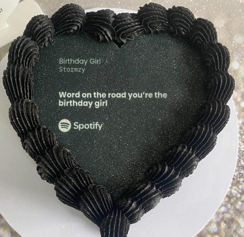 Pode incluir: Um bolo em forma de cora&ccedil;&atilde;o com cobertura preta e uma superf&iacute;cie preta brilhante. O bolo tem o texto "Birthday Girl Stormzy" e "Word on the road you're the birthday girl" com o logotipo do Spotify.