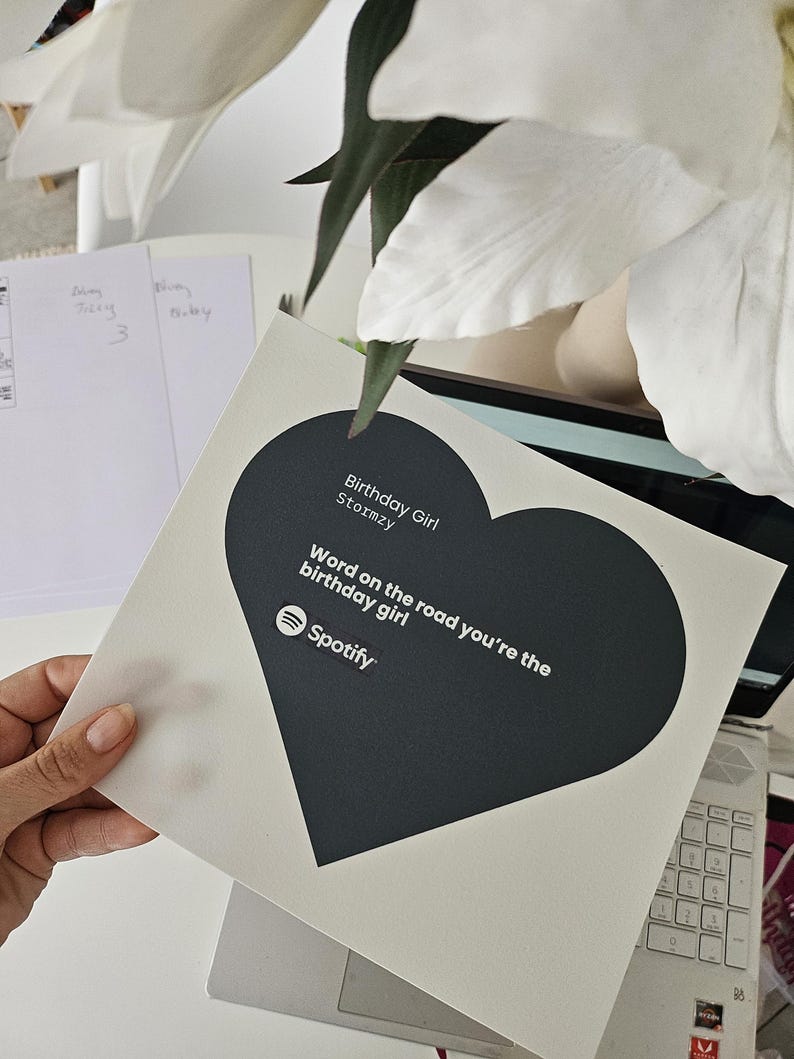 Pode incluir: Um cart&atilde;o branco com um design em forma de cora&ccedil;&atilde;o preto. O cart&atilde;o apresenta o texto "Birthday Girl Stormzy" e "Word on the road you're the birthday girl" com o logotipo do Spotify. O cart&atilde;o &eacute; segurado por uma m&atilde;o.