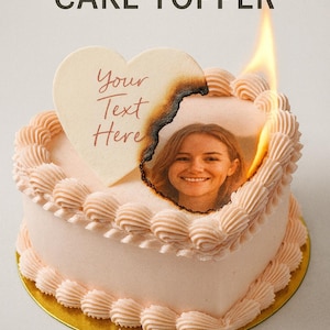 Puede incluir: Un pastel en forma de corazón con foto y texto personalizados, coronado con un diseño de papel de oblea en llamas. El pastel está decorado con glaseado rosa y una base dorada. El texto en el pastel dice "BURN-AWAY CAKE TOPPER" y "Your Text Here".