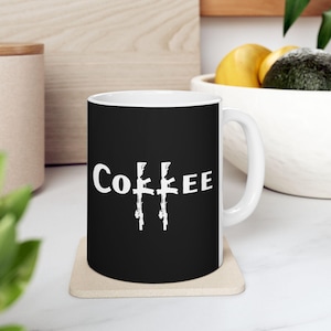 May include: A black coffee mug with a white design of three rifles and the word "COFFEE" printed on it.