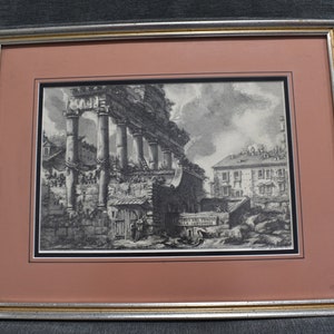 May include: A black and white etching of a Roman ruin with columns and a building in the background. The etching is framed in a gold and silver frame.