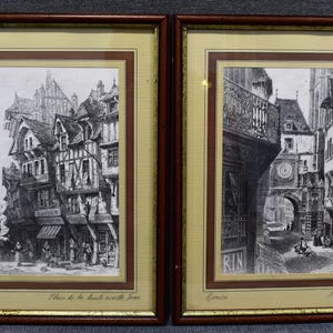 Può includere: Due stampe in bianco e nero incorniciate di edifici storici in una città europea. Le stampe sono in cornici ornate con finiture dorate. La prima stampa è intitolata "Place de la Louche avec son pont" e la seconda stampa è intitolata "Le grand hourloge".