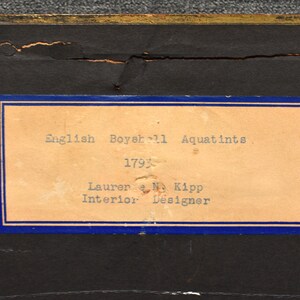 May include: A close-up of a label with blue trim and white text. The label reads "English Boyer 11 Aquatints 1793 Lauren & M. Kipp Interior Designer".