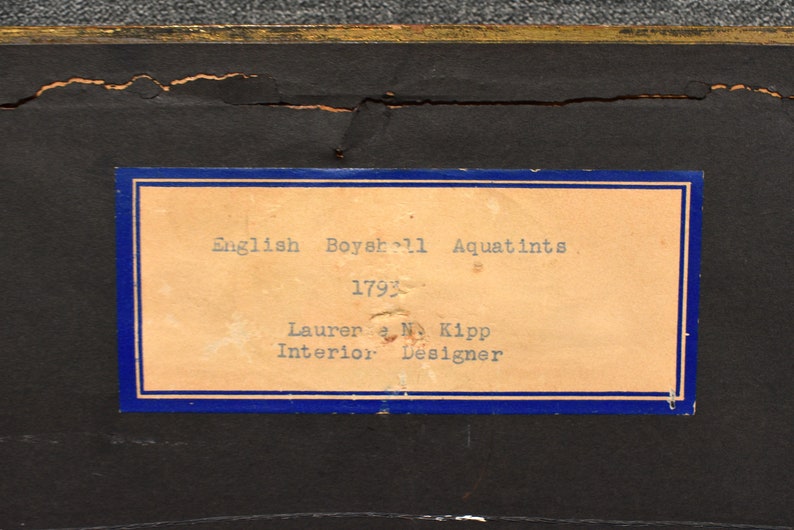 May include: A close-up of a label with blue trim and white text. The label reads "English Boyer 11 Aquatints 1793 Lauren & M. Kipp Interior Designer".