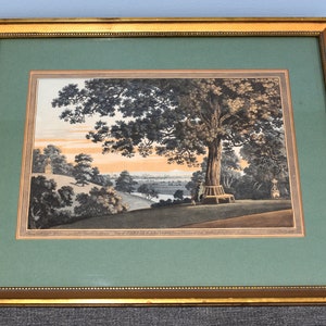 May include: A framed print of a landscape scene with a large tree in the foreground, a winding path, and a distant town. The print is in shades of brown, green, and blue, and has a gold frame.