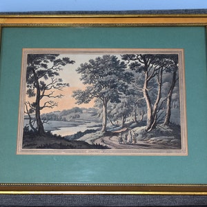 May include: A framed print of a landscape scene with trees, a river, and figures in the distance. The print is in a gold frame with a green mat.