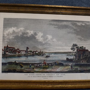 Op de afbeelding: Een antieke prent die een uitzicht toont op een deel van de stad Chalon-sur-Saône, Frankrijk. De prent toont de stad vanaf de andere kant van de Saône, met de kathedraal en het Hôtel-Dieu in de verte. De prent is in zwart-wit met handgekleurde details.