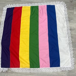 Peut inclure: Un tissu rayé coloré avec une bordure en dentelle blanche. Le tissu est fait d'un matériau doux et tissé et présente un arc-en-ciel de couleurs, notamment le violet, le rouge, le jaune, le vert, le rose et le bleu.