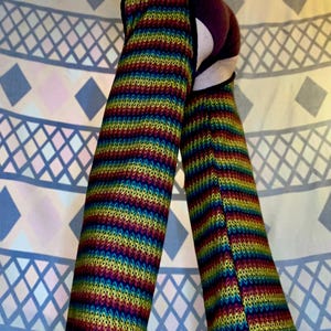 May include: A pair of colorful striped leg warmers with a cutout in the back. The leg warmers are made of a knitted fabric and have a rainbow pattern.