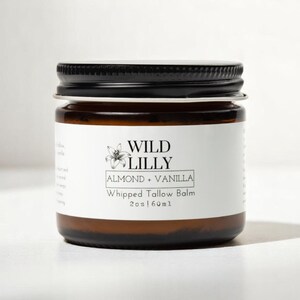 K&ouml;nnte beinhalten: Ein braunes Glasgef&auml;&szlig; mit schwarzem Deckel, gef&uuml;llt mit Wild Lilly Mandel & Vanille Schlagsahne-Talg-Balsam, 2 oz / 60 ml.