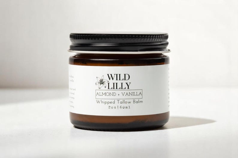 K&ouml;nnte beinhalten: Ein braunes Glasgef&auml;&szlig; mit schwarzem Deckel, gef&uuml;llt mit Wild Lilly Mandel & Vanille Schlagsahne-Talg-Balsam, 2 oz / 60 ml.