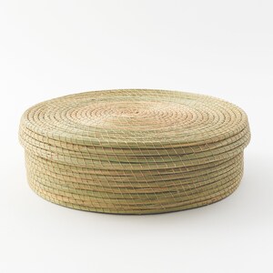 May include: A round, woven basket made of natural materials. The basket is light brown and has a natural, rustic look.
