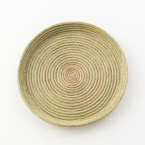 May include: A round woven tray made of natural materials, with a light brown color and a circular pattern.