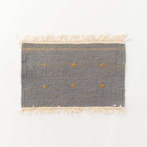 May include: A gray woven rug with a fringe border and small yellow squares throughout.