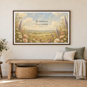 May include: A rectangular framed wall art print featuring a landscape painting of a rolling meadow filled with wildflowers under a cloudy sky. The text "By wisdom a house is built" is centred in the upper portion of the print in dark lettering.