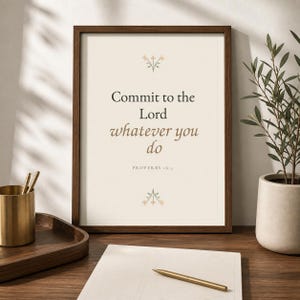 May include: A framed wall art print featuring the text Commit to the Lord whatever you do Proverbs 16:3 in dark brown and tan serif fonts. The design includes small floral illustrations above and below the text on a cream background.
