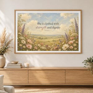 以下が含まれることがあります： 雲のある青い空の下に広がる野草の草原を描いた、額装された風景画のウォールアートプリント。テキストには「She is clothed with strength and dignity, Proverbs 31:25」と書かれています。アートワークは明るい木製のフレームに入っています。