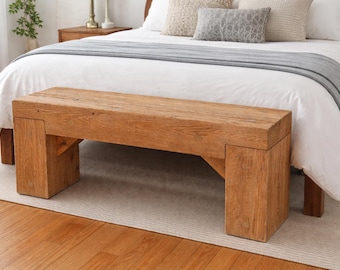 May include: A rustic wooden bench with a natural finish. The bench is rectangular with thick legs and a solid top. It is placed at the foot of a bed with white bedding and decorative pillows. The bench is approximately 60 inches long.