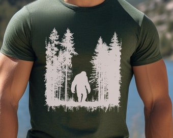 May include: A green t-shirt with a white silhouette of Bigfoot walking through a forest. The t-shirt has a distressed, vintage look.