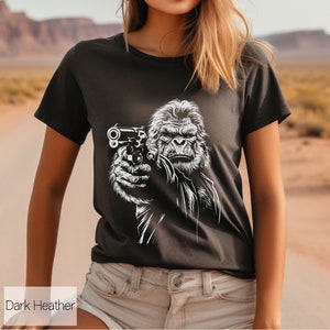 以下が含まれることがあります： 暗いヘザーグレーのTシャツに、銃を持ったゴリラの白いグラフィックがプリントされています。